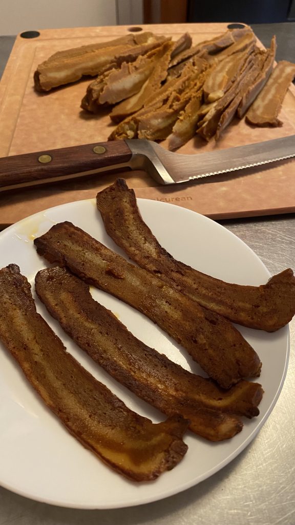 cooked seitan bacon in the front and sliced seitan bacon in the back